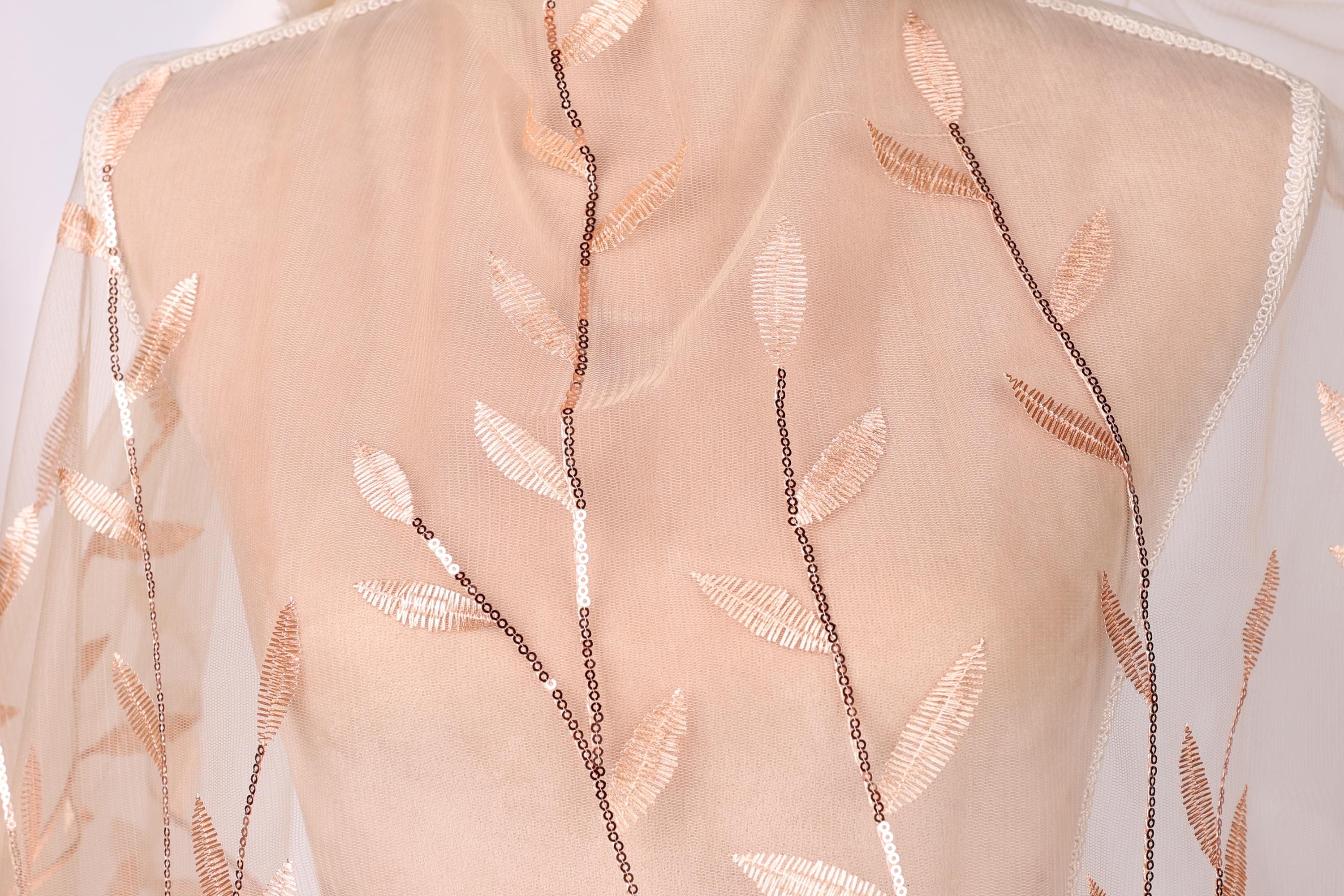 A mannequin wearing a sheer, peach-colored dress with delicate leaf-like embroidered patterns.