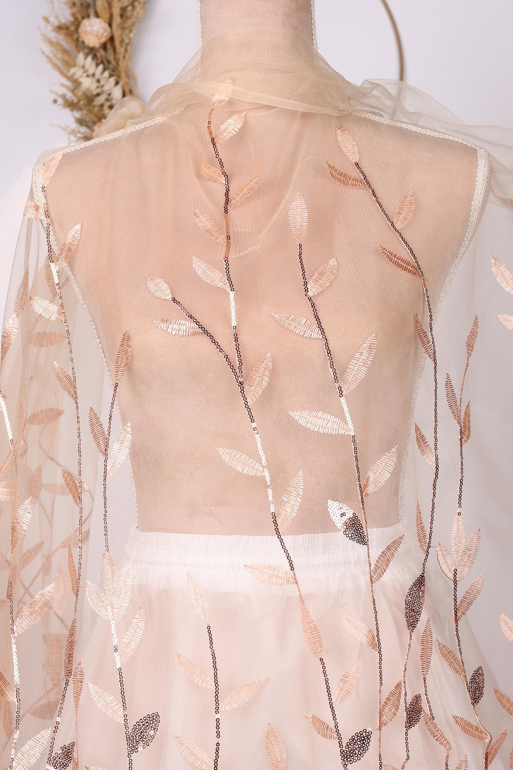 a mannequin wearing a white dress with a sheer, floral-patterned fabric draped over it. The dress has a delicate, lace-like design with a floral motif.