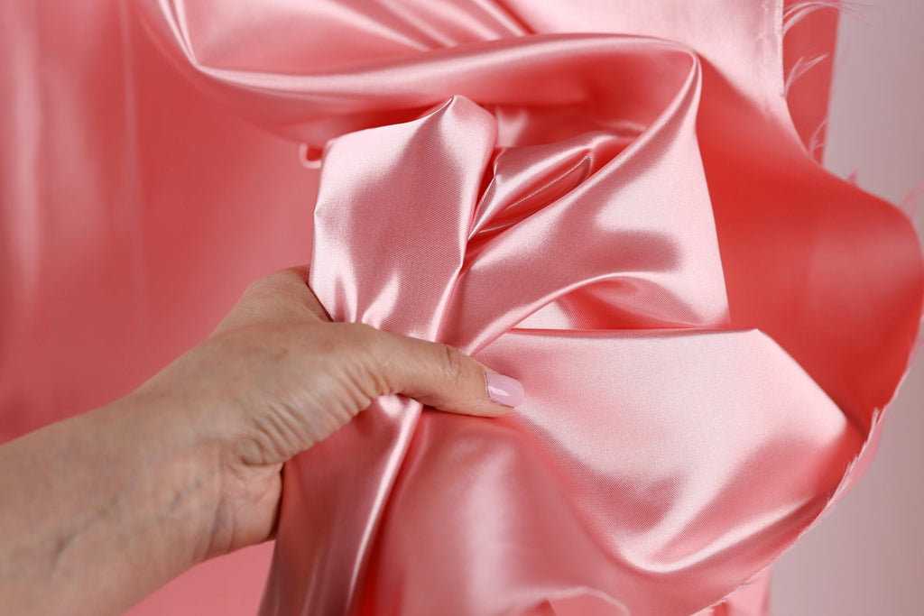 A hand is holding a piece of pink satin fabric, examining it closely.