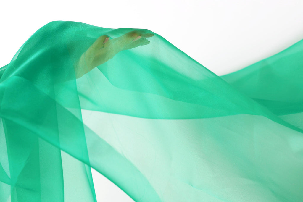a hand holding a green fabric, which appears to be flowing or billowing in the air.