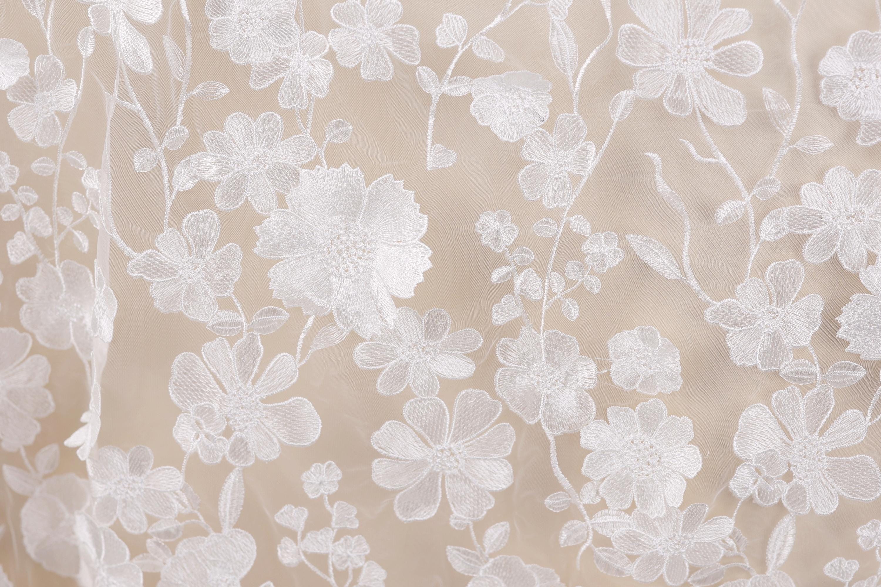 a close-up view of a delicate, white lace fabric with a floral pattern. The lace appears to be made of a soft, delicate material, and the intricate design of the flowers and leaves creates a visually appealing and elegant appearance.
