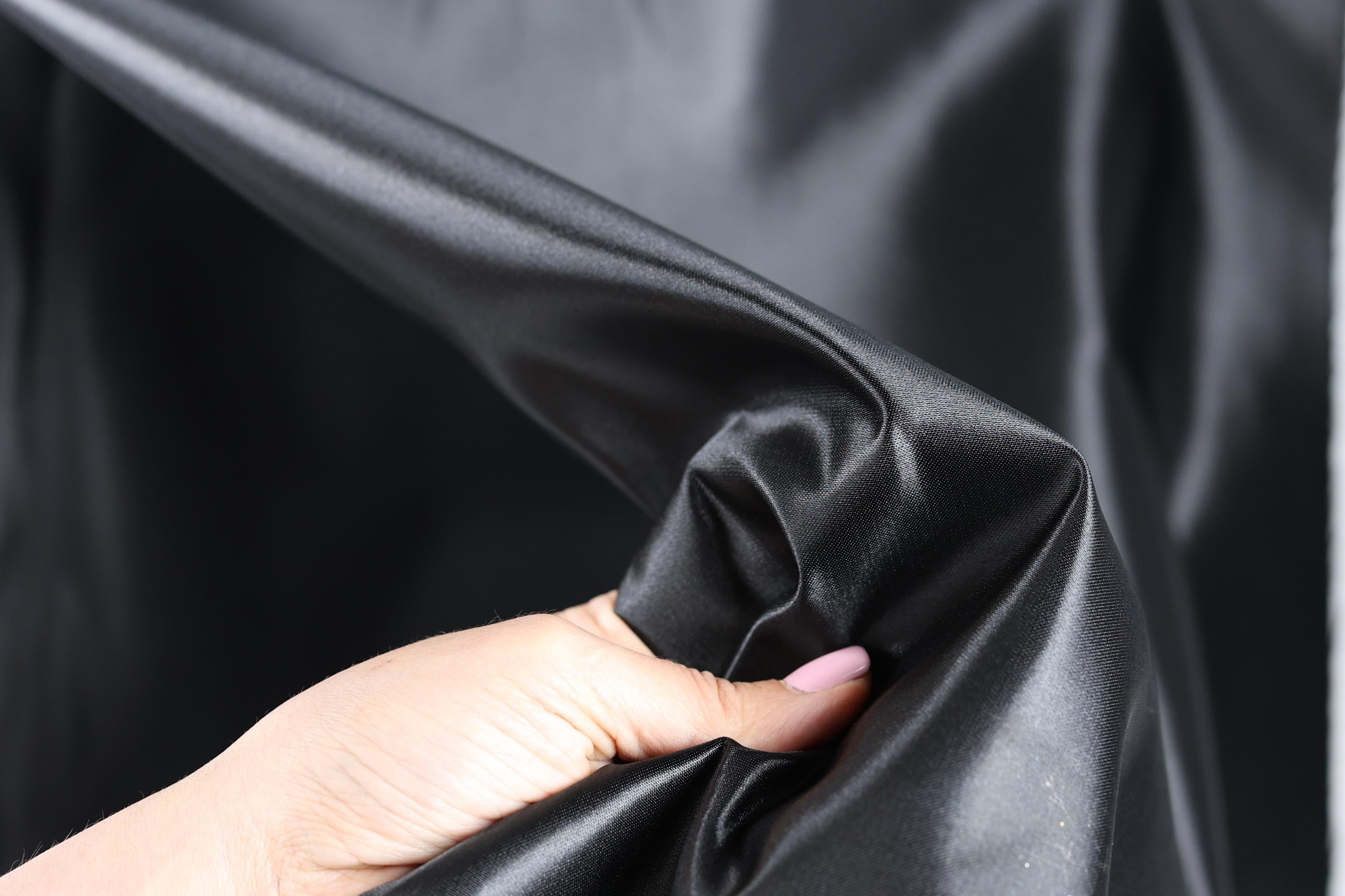 A hand is holding a piece of black fabric, which appears to be shiny and smooth.