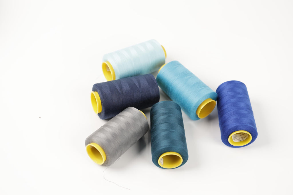 a collection of six spools of thread in various colors, including blue, gray, and yellow, arranged on a white background.