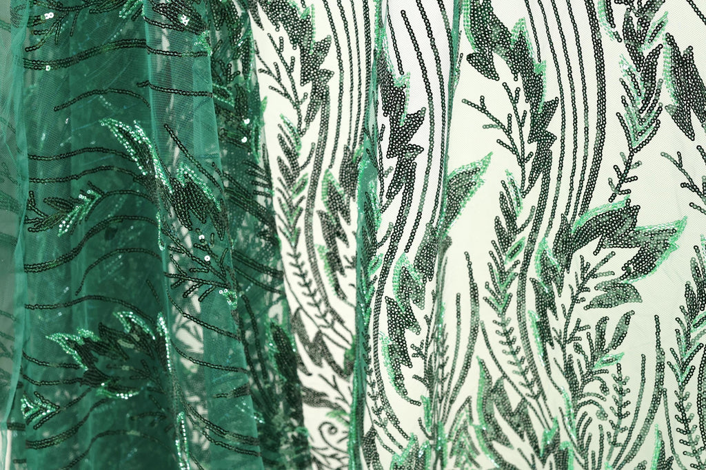 a close-up view of a fabric with a green and black leaf pattern. The fabric appears to be made of a sheer material, with a repeating pattern of green leaves and black lines. The leaves are arranged in a vertical orientation, creating a sense of depth and texture in the image.