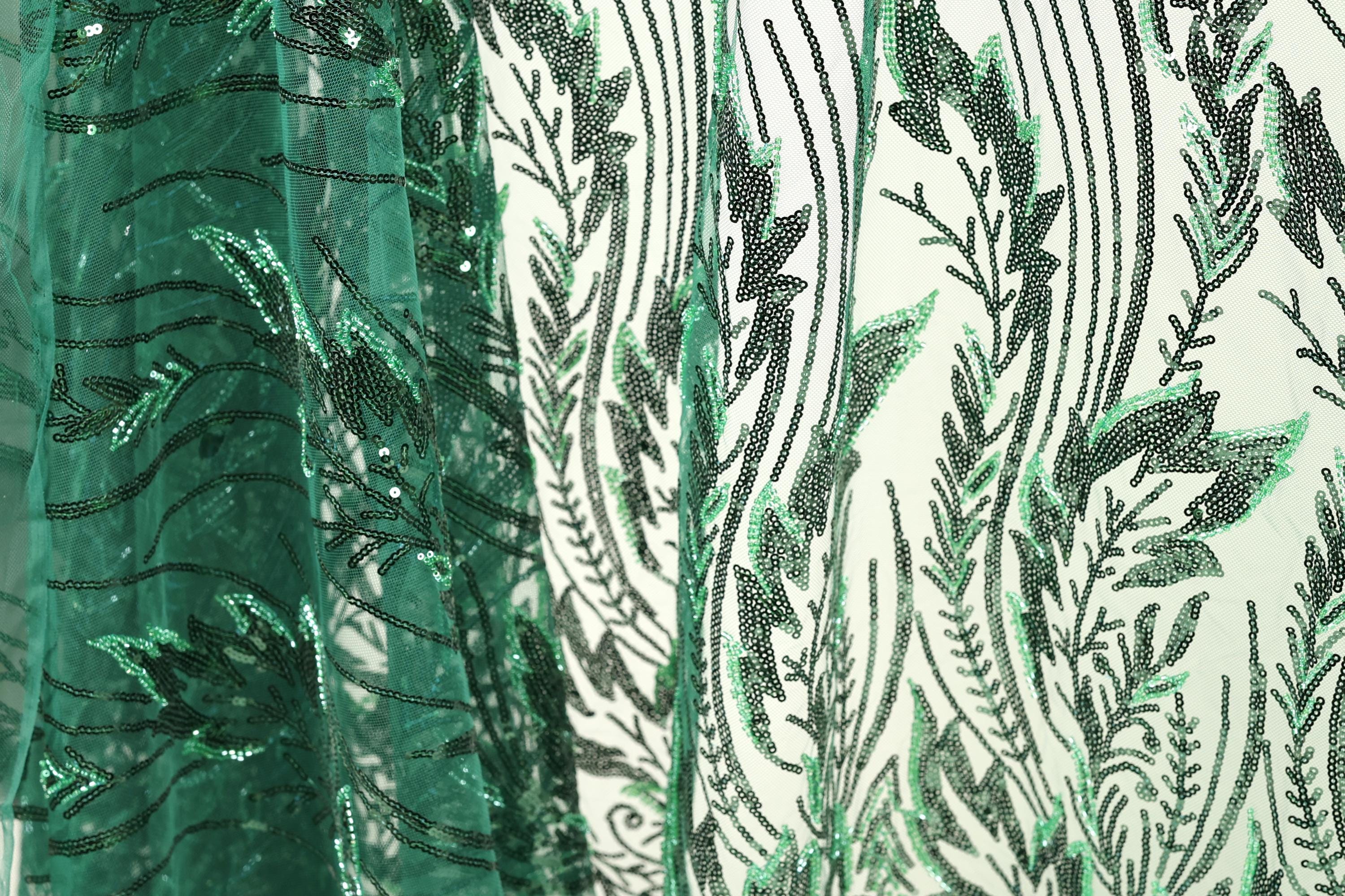 a close-up view of a fabric with a green and black leaf pattern. The fabric appears to be made of a sheer material, with a repeating pattern of green leaves and black lines. The leaves are arranged in a vertical orientation, creating a sense of depth and texture in the image.