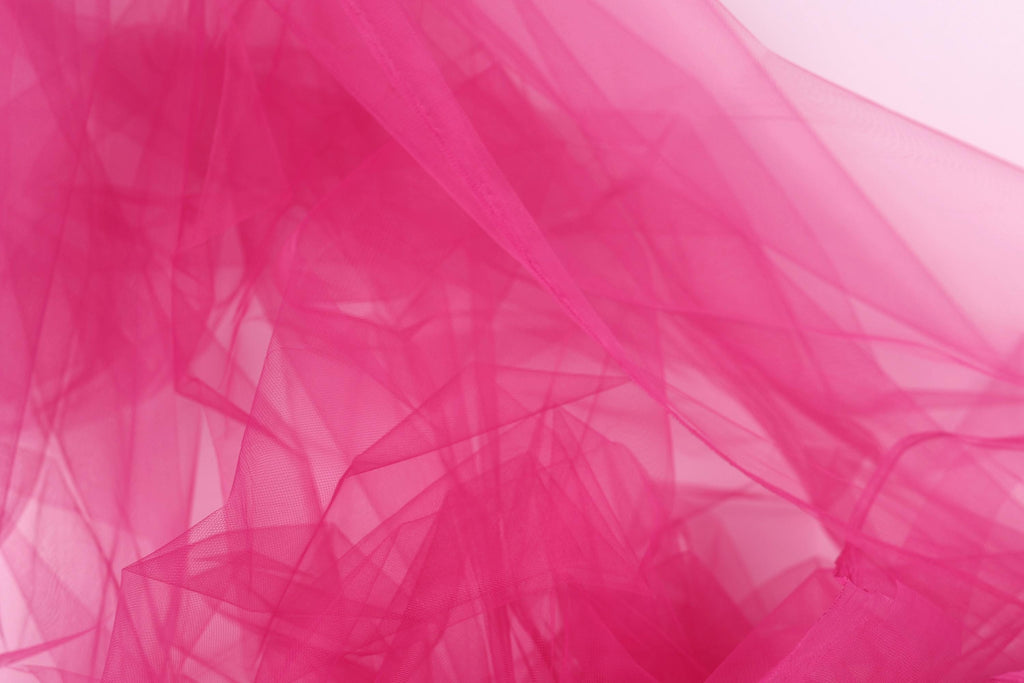The image is a close-up of a pink, sheer fabric, possibly tulle, with a soft, flowing texture.