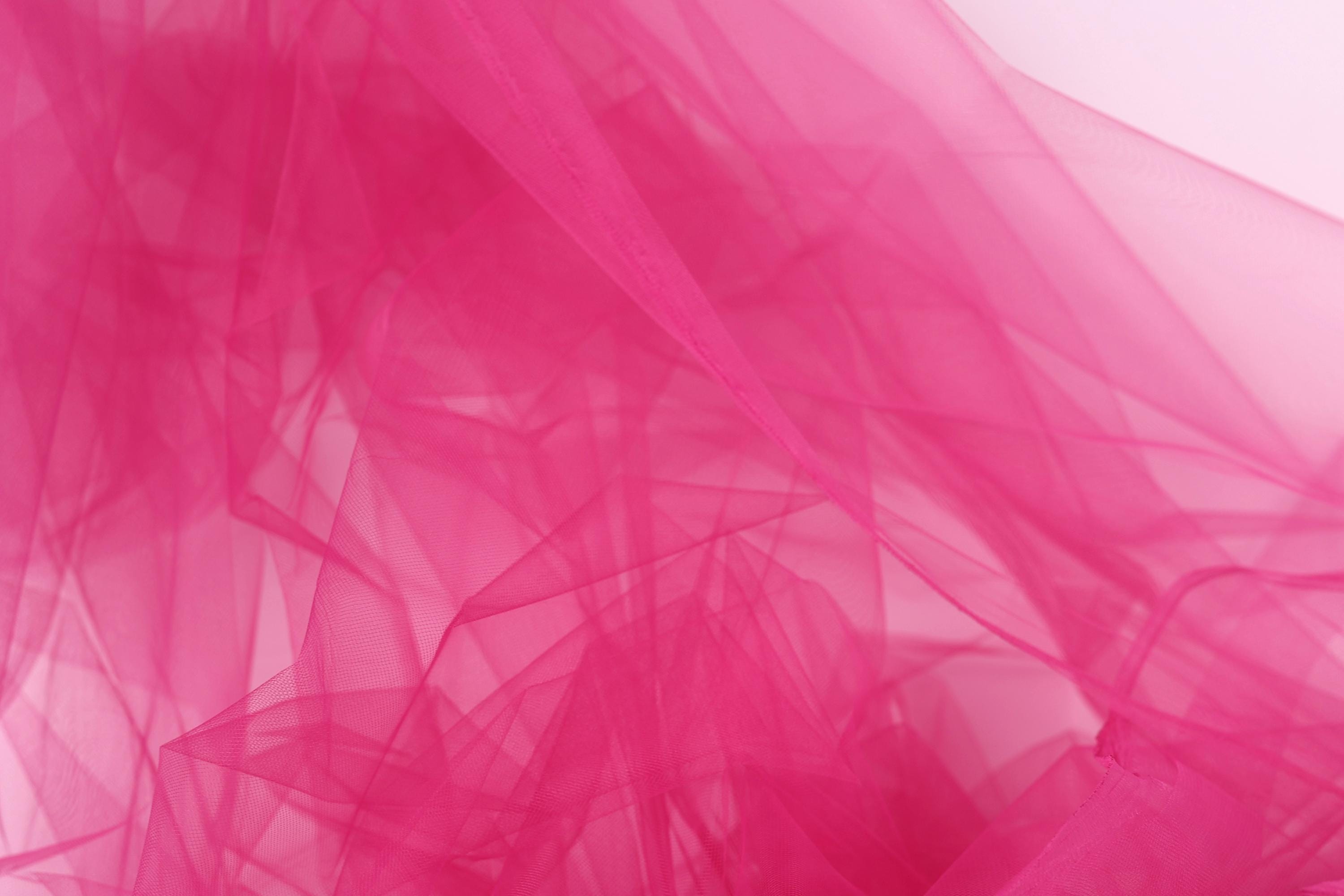 The image is a close-up of a pink, sheer fabric, possibly tulle, with a soft, flowing texture.
