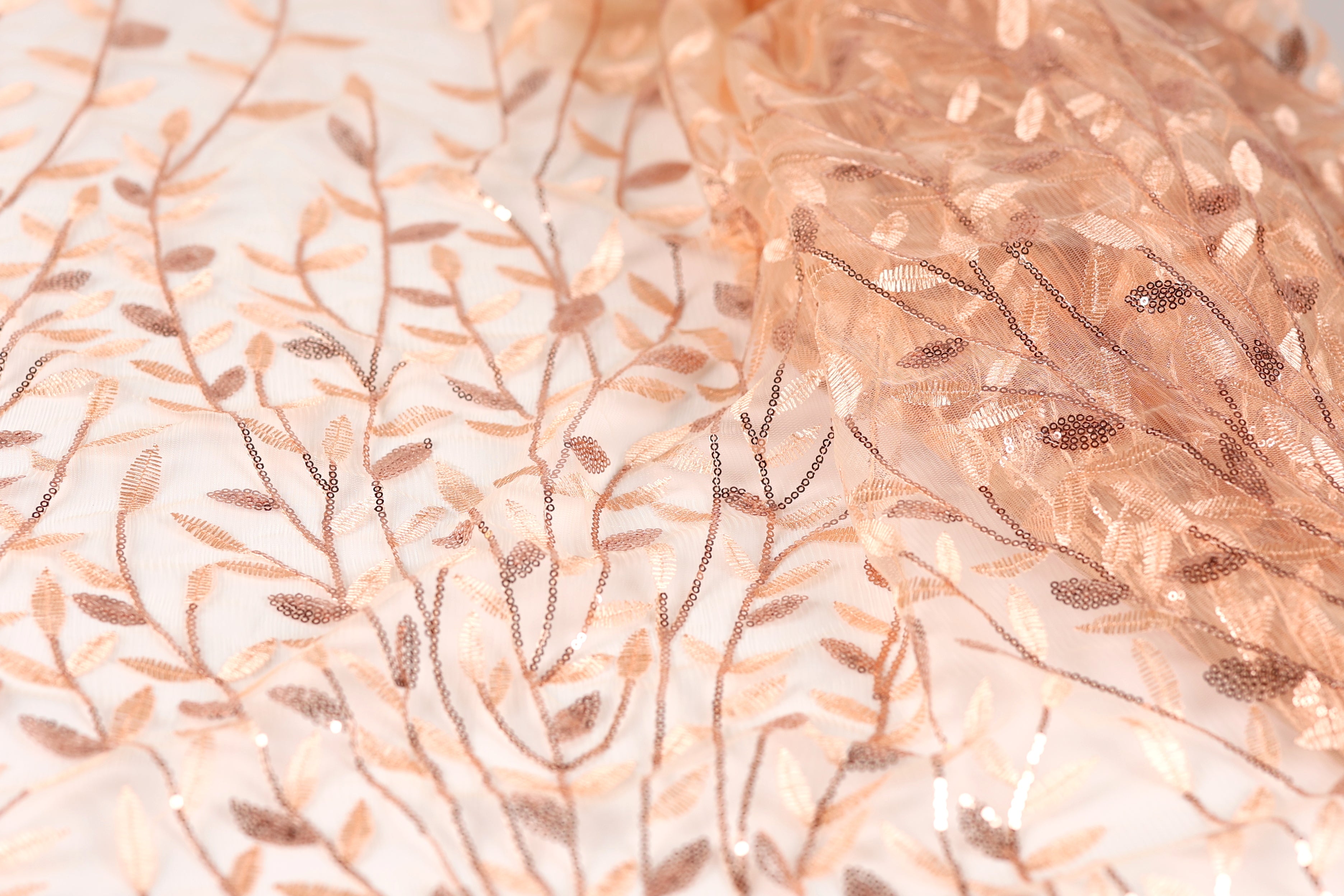 a close-up view of a fabric with a delicate, intricate floral pattern. The fabric appears to be made of a light-colored material, possibly silk or chiffon, with a subtle, shimmering texture. The pattern consists of numerous small, thin, and delicate leaves and branches, creating a visually appealing and delicate design.