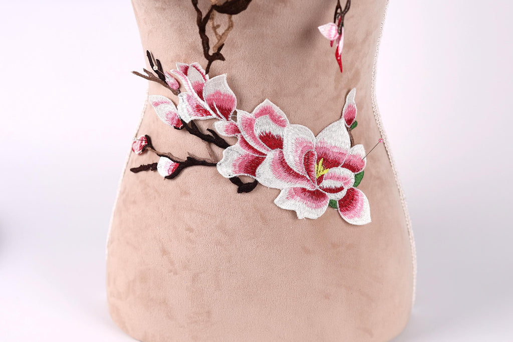 A close-up image of a beige fabric with a floral embroidered design featuring pink and white flowers.