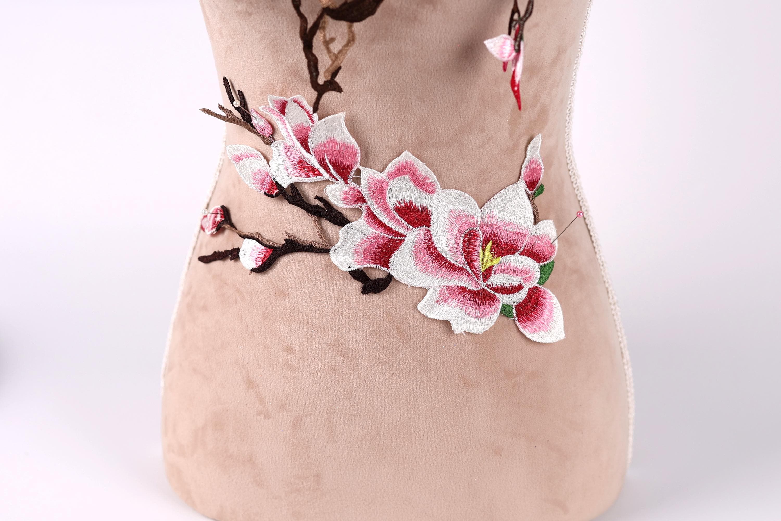 A close-up image of a beige fabric with a floral embroidered design featuring pink and white flowers.