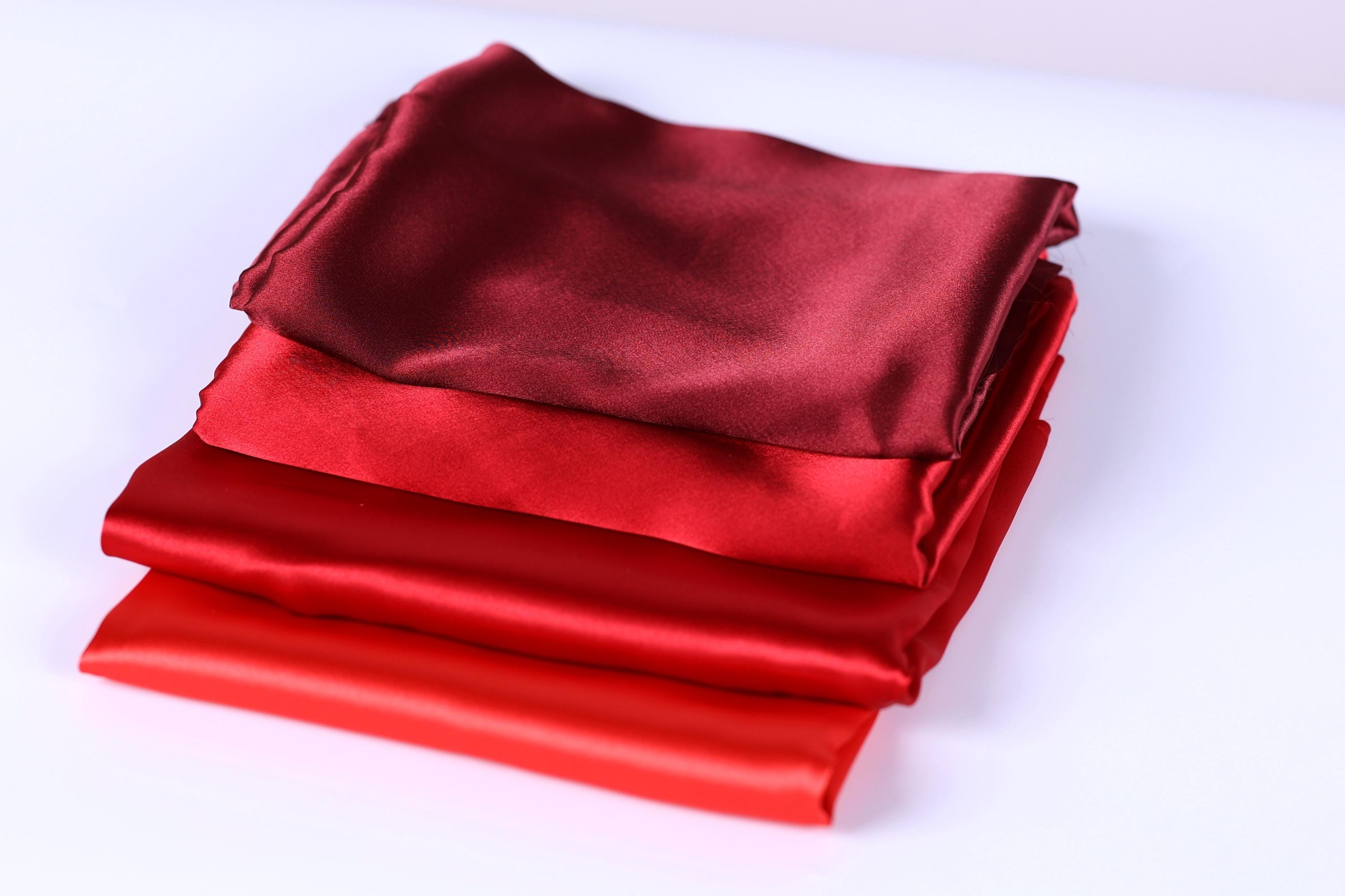 A stack of four red satin fabric pieces is neatly arranged on a white surface.