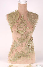 A mannequin with a beige body and gold embroidered details, including floral and leaf patterns, as well as sequin accents.