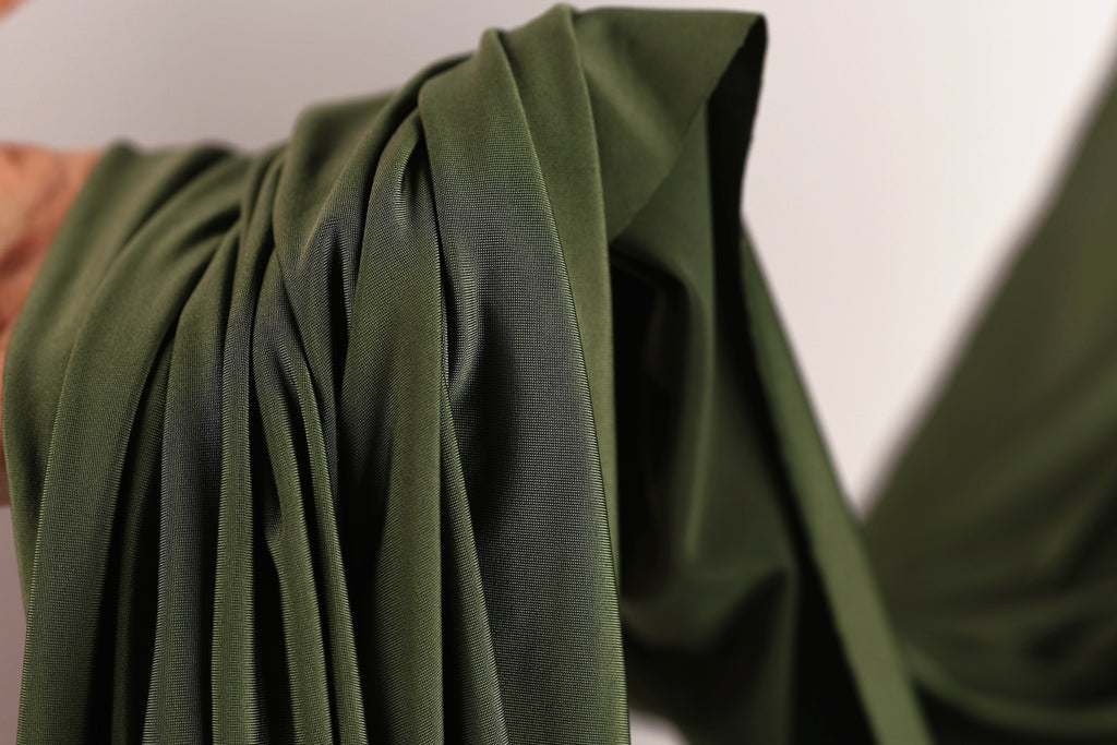 A close-up view of a green fabric, possibly a piece of clothing or a textile, with a blurred background.