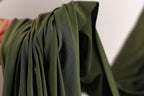 A close-up view of a green fabric, possibly a piece of clothing or a textile, with a blurred background.