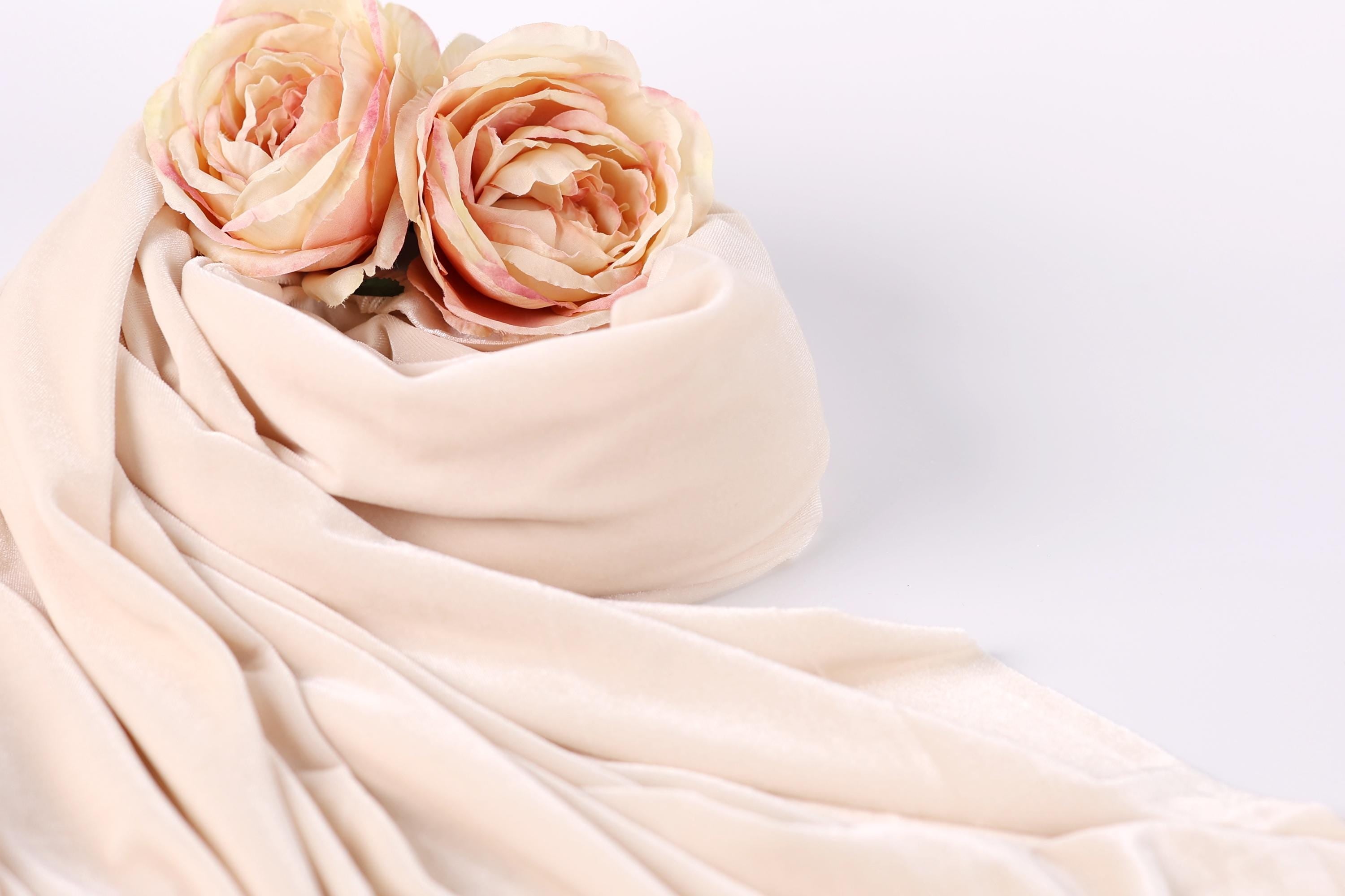 A pair of pink roses rests on a soft, flowing beige fabric, creating a serene and elegant scene.
