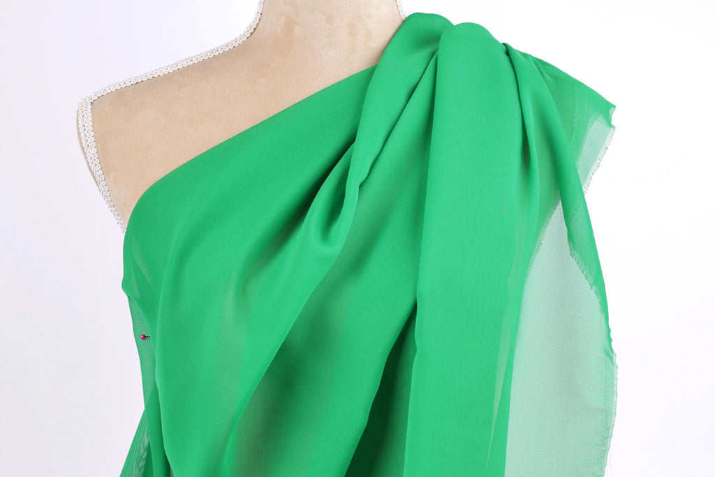 A mannequin wearing a green one-shoulder dress with a draped, flowing fabric.