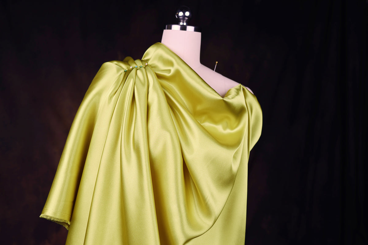 A mannequin wearing a bright yellow satin dress with a draped, flowing silhouette.