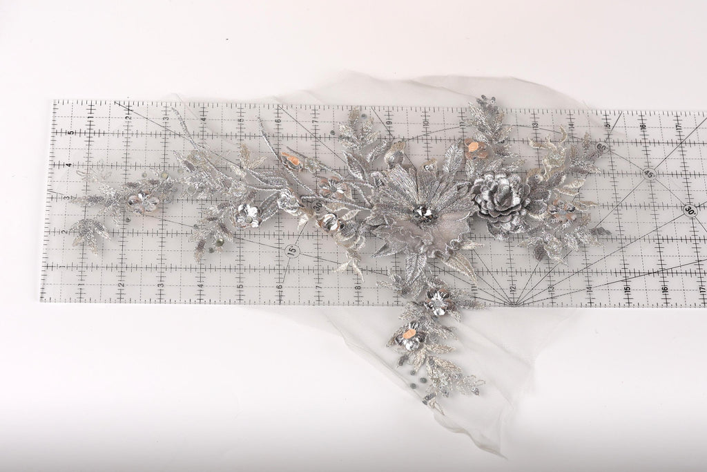a decorative silver floral piece with intricate details, including leaves, flowers, and a central flower, all set against a white background.