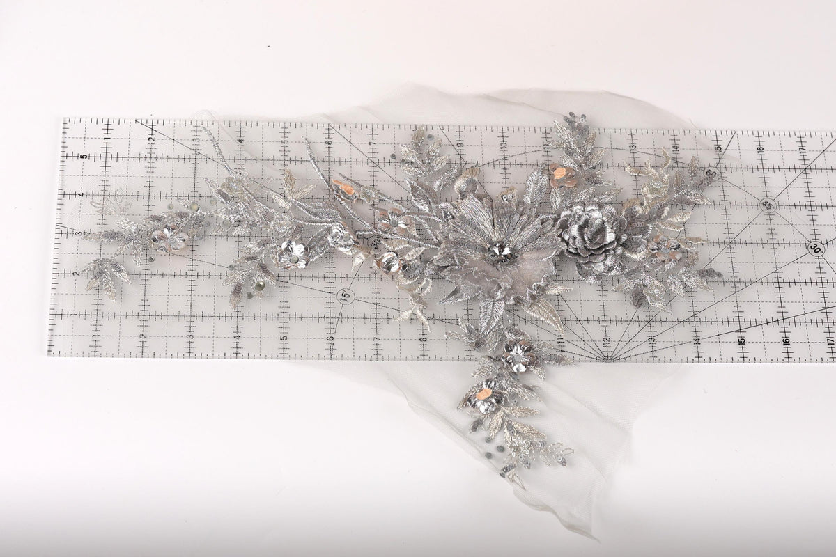 a decorative silver floral piece with intricate details, including leaves, flowers, and a central flower, all set against a white background.
