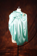 A mannequin wearing a turquoise satin garment stands against a brown background.