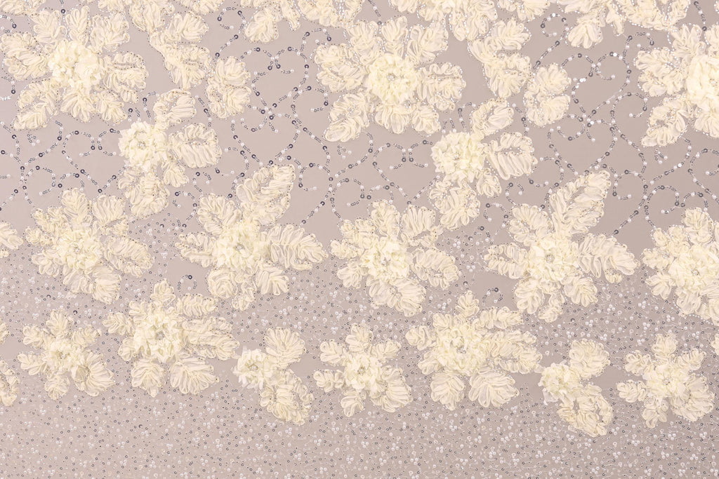 a close-up view of a fabric with a floral pattern. The fabric appears to be made of a light-colored material, possibly lace or a similar type of material. The pattern consists of numerous small white flowers or leaves scattered across the fabric, creating a visually appealing and intricate design. The image does not contain any text or other discernible objects, and the focus is solely on the floral pattern on the fabric.