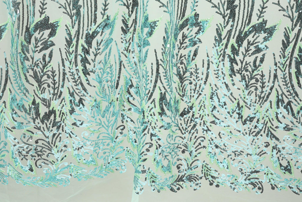 a close-up view of a fabric with a repeating pattern of green and black sequin designs. The pattern appears to be a floral or leaf-like design, with the sequins arranged in a way that creates a sense of depth and texture. The fabric has a light green background, which contrasts with the dark green and black sequin pattern. The image does not contain any text or other discernible objects, and the focus is solely on the intricate and detailed design of the fabric.