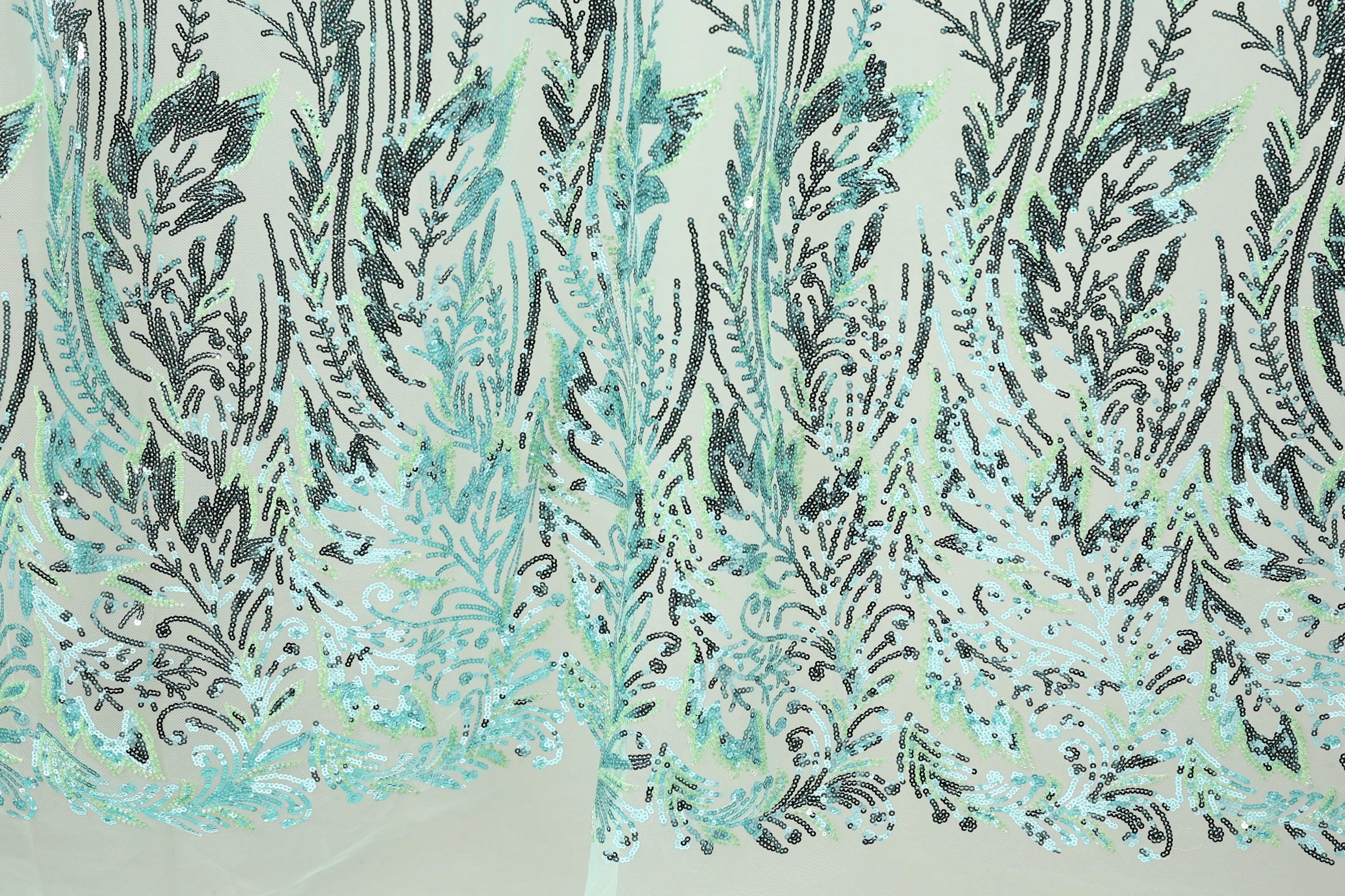 a close-up view of a fabric with a repeating pattern of green and black sequin designs. The pattern appears to be a floral or leaf-like design, with the sequins arranged in a way that creates a sense of depth and texture. The fabric has a light green background, which contrasts with the dark green and black sequin pattern. The image does not contain any text or other discernible objects, and the focus is solely on the intricate and detailed design of the fabric.