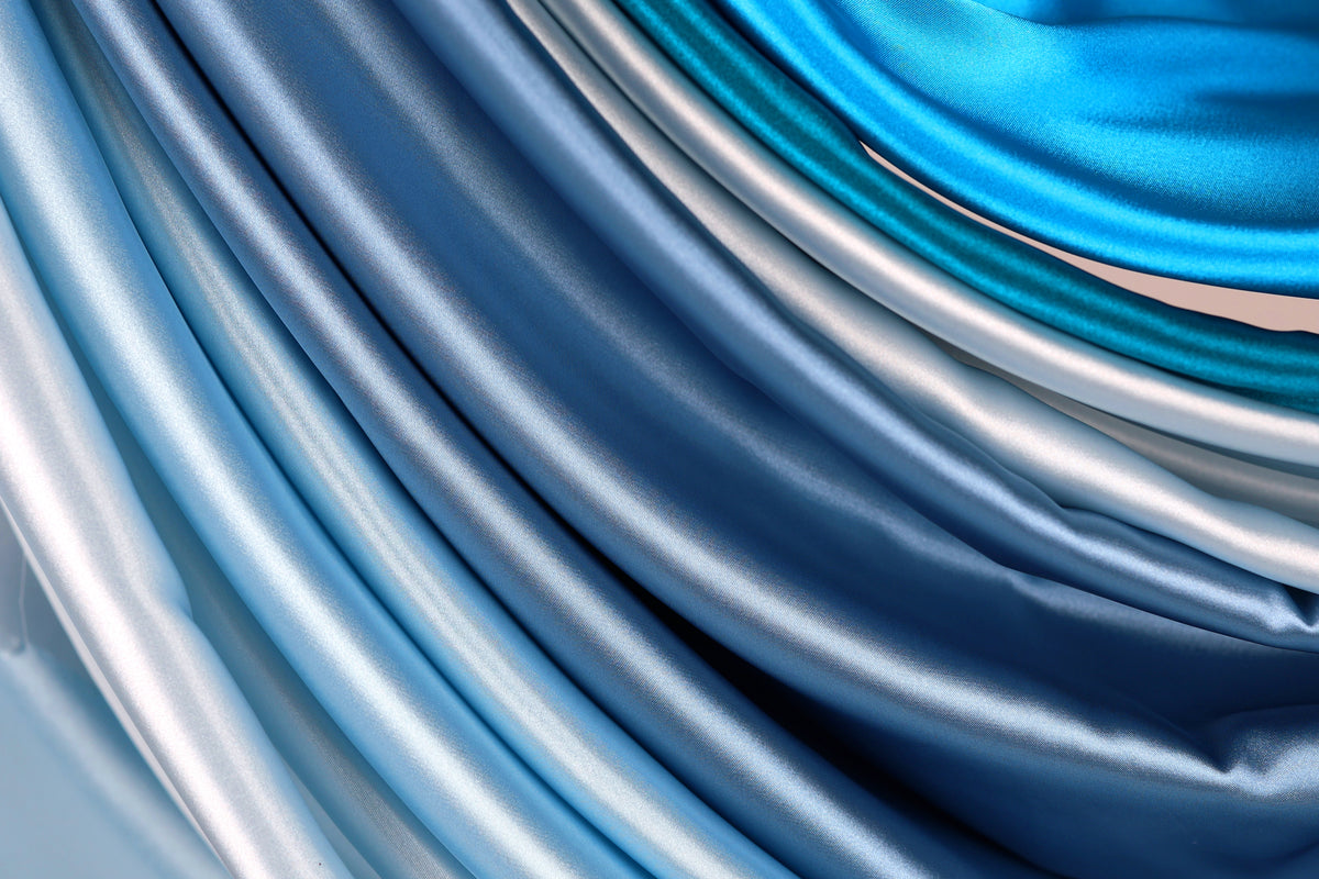 a close-up view of a collection of blue and silver satin fabric, with the fabric appearing to be folded or draped in a way that creates a sense of movement and texture.