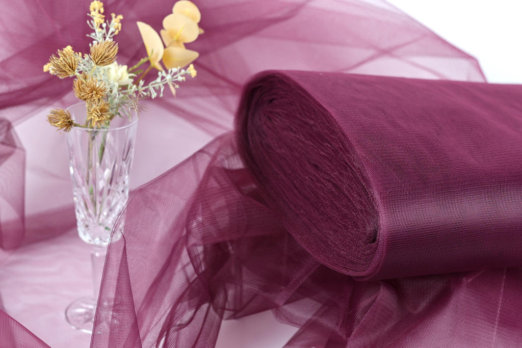 a clear glass vase filled with yellow flowers, placed on a purple fabric or sheer material.