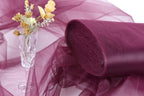 a clear glass vase filled with yellow flowers, placed on a purple fabric or sheer material.