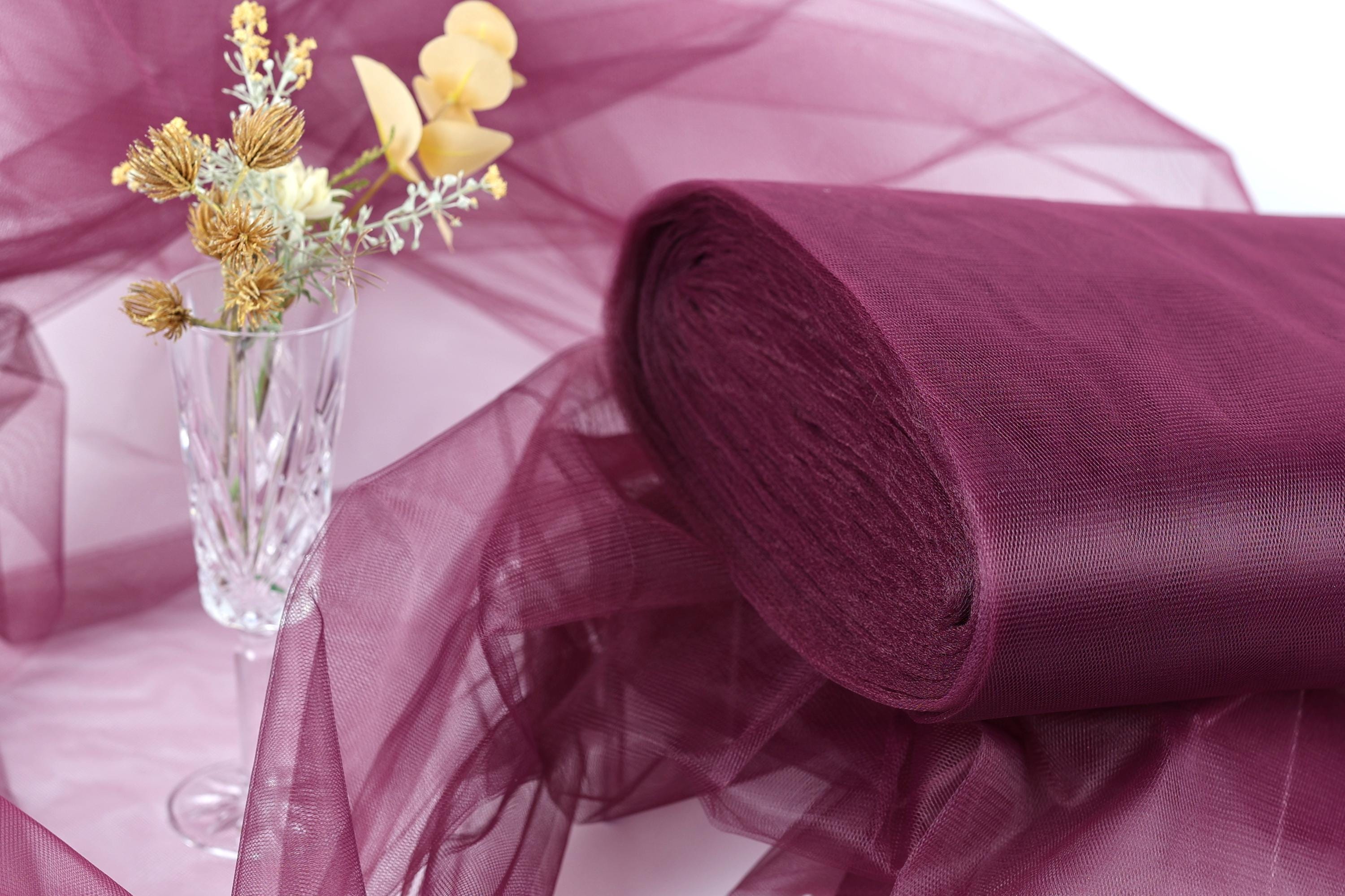 a clear glass vase filled with yellow flowers, placed on a purple fabric or sheer material.