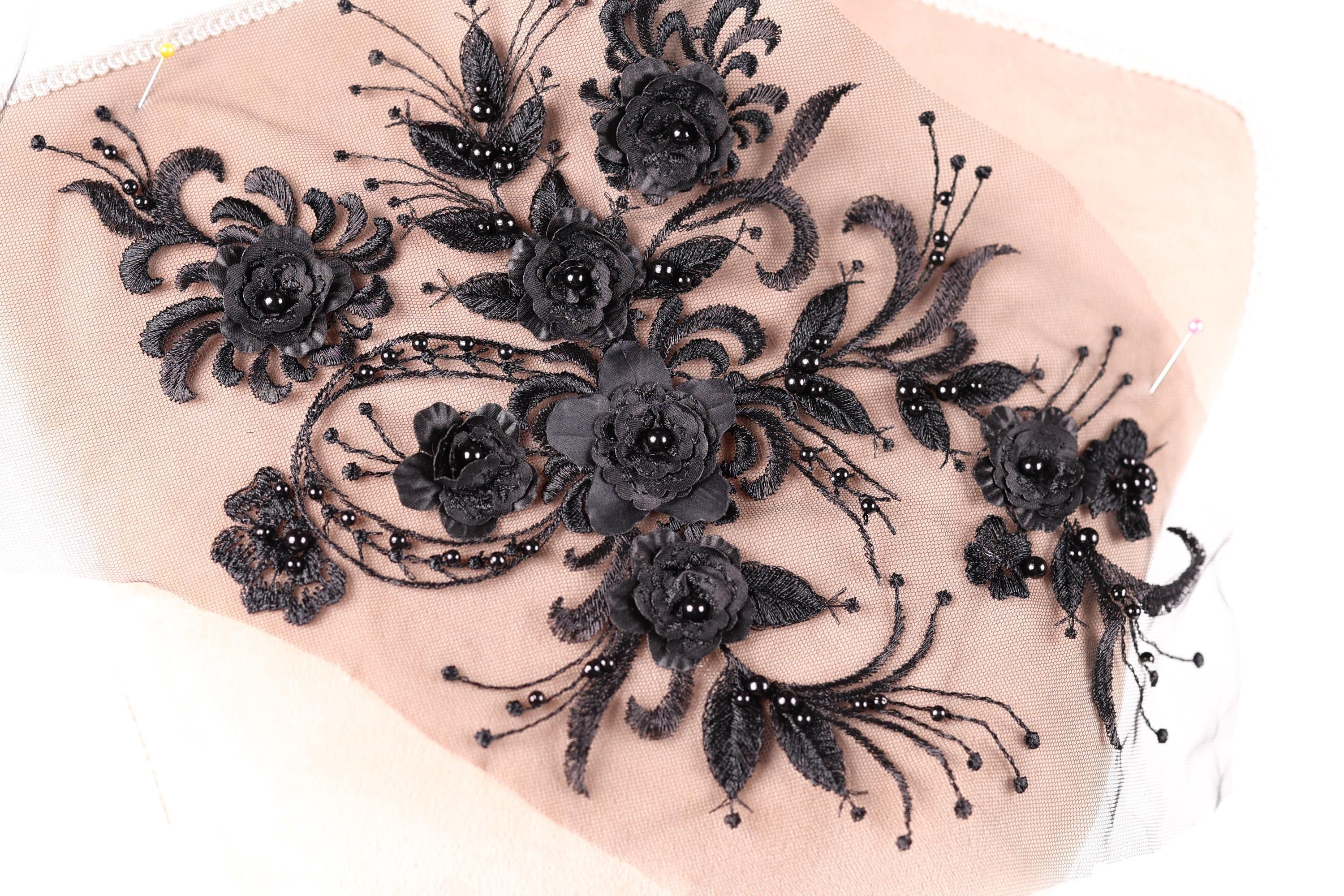 a close-up view of a delicate, intricate black lace design with numerous black flowers and leaves. The design is detailed and ornate, showcasing the craftsmanship and artistry involved in creating such a piece.
