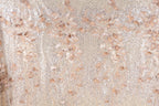 a close-up view of a fabric with a floral pattern, including leaves and flowers. The fabric appears to be made of a shiny, glittery material, giving it a sparkly and elegant appearance.