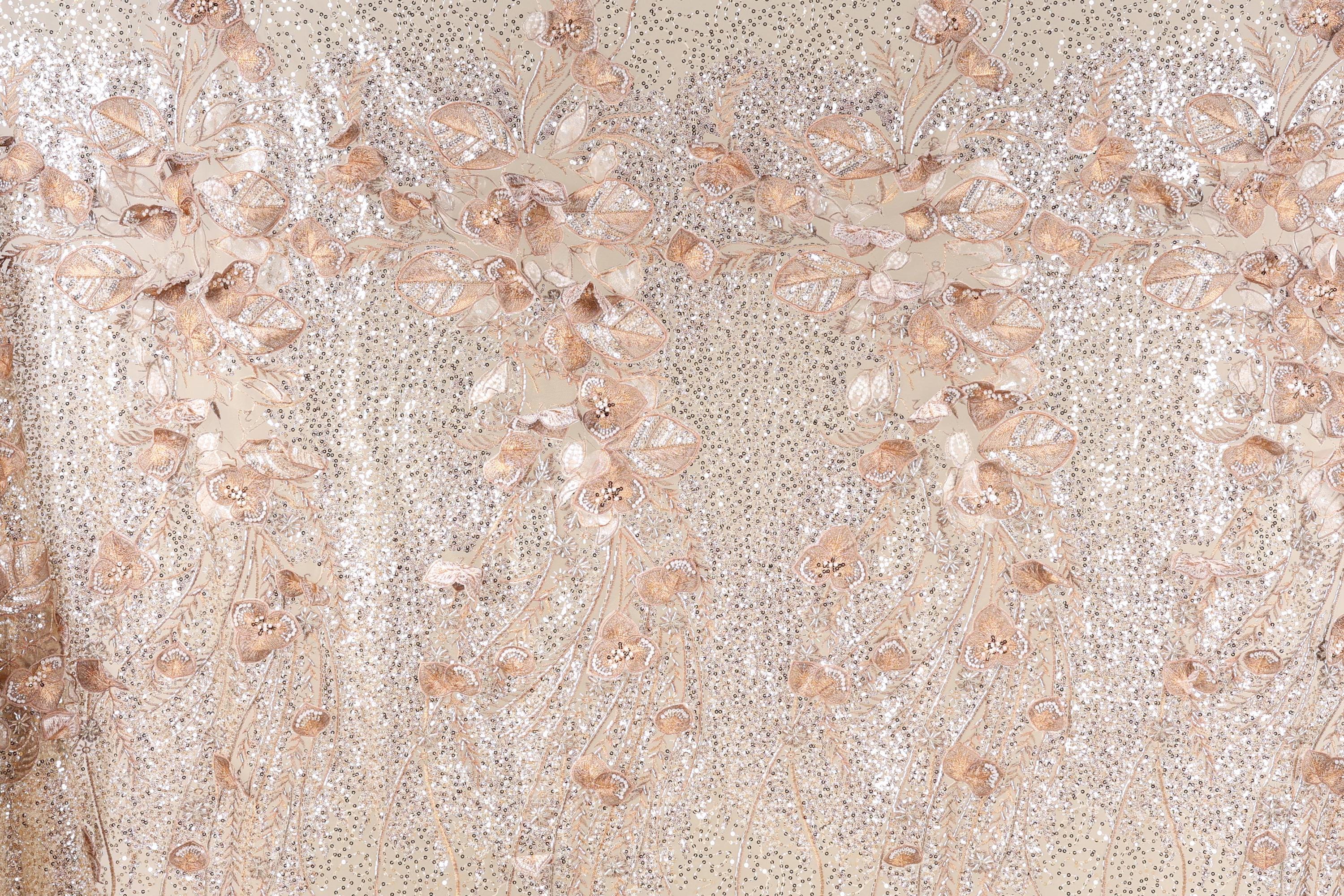 a close-up view of a fabric with a floral pattern, including leaves and flowers. The fabric appears to be made of a shiny, glittery material, giving it a sparkly and elegant appearance.