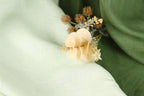 A close-up image of a delicate flower with pale yellow petals, resting on a soft, blurred green fabric.