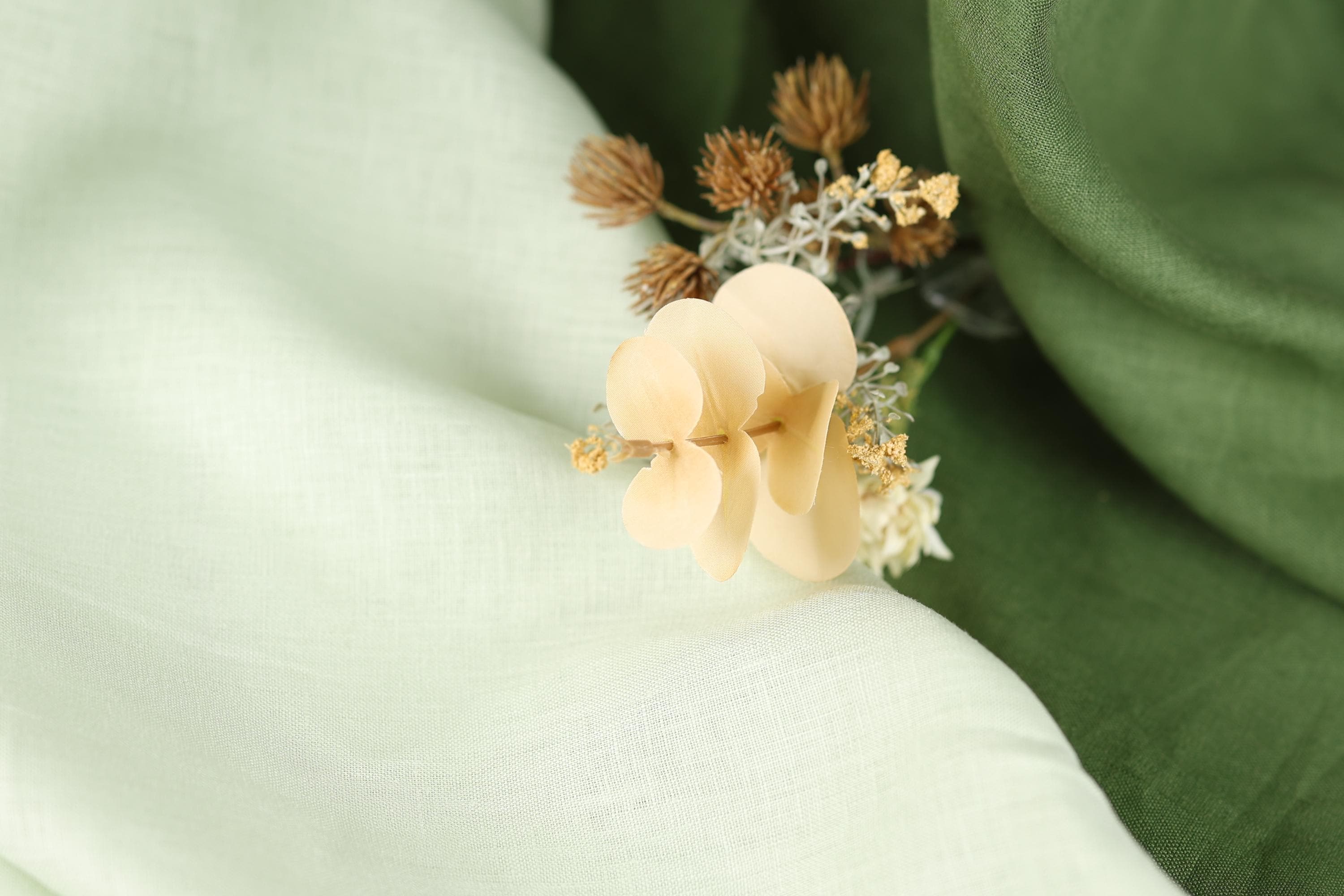 A close-up image of a delicate flower with pale yellow petals, resting on a soft, blurred green fabric.