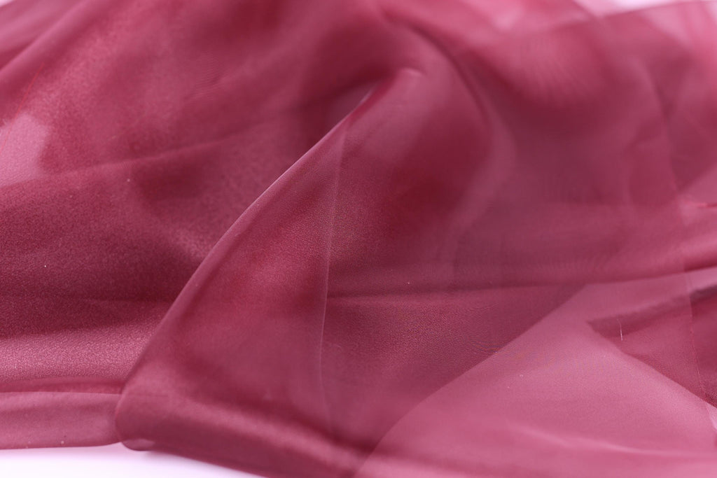 The image is a close-up of a soft, flowing fabric in a deep red color, with a slightly wrinkled texture.