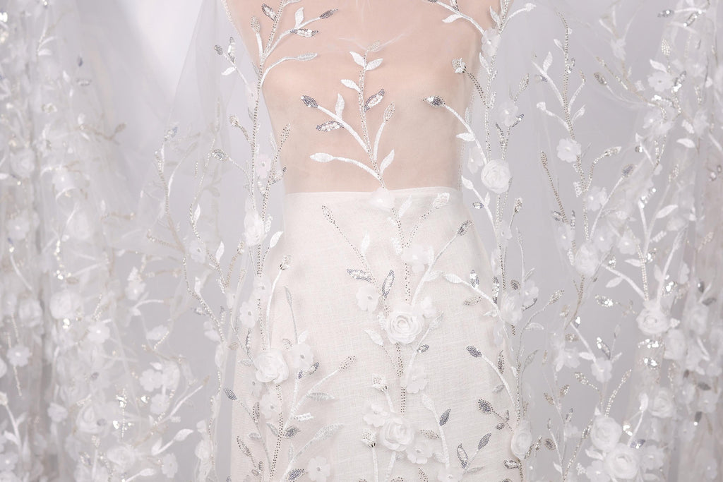 A white dress with a sheer, lace-like fabric draped over it, featuring delicate floral patterns.
