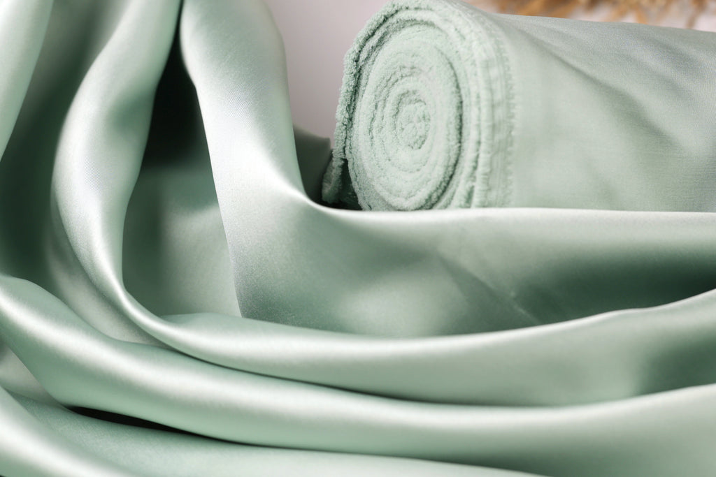 A close-up view of a piece of green satin fabric, with a rolled-up end visible.