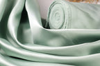 A close-up view of a piece of green satin fabric, with a rolled-up end visible.