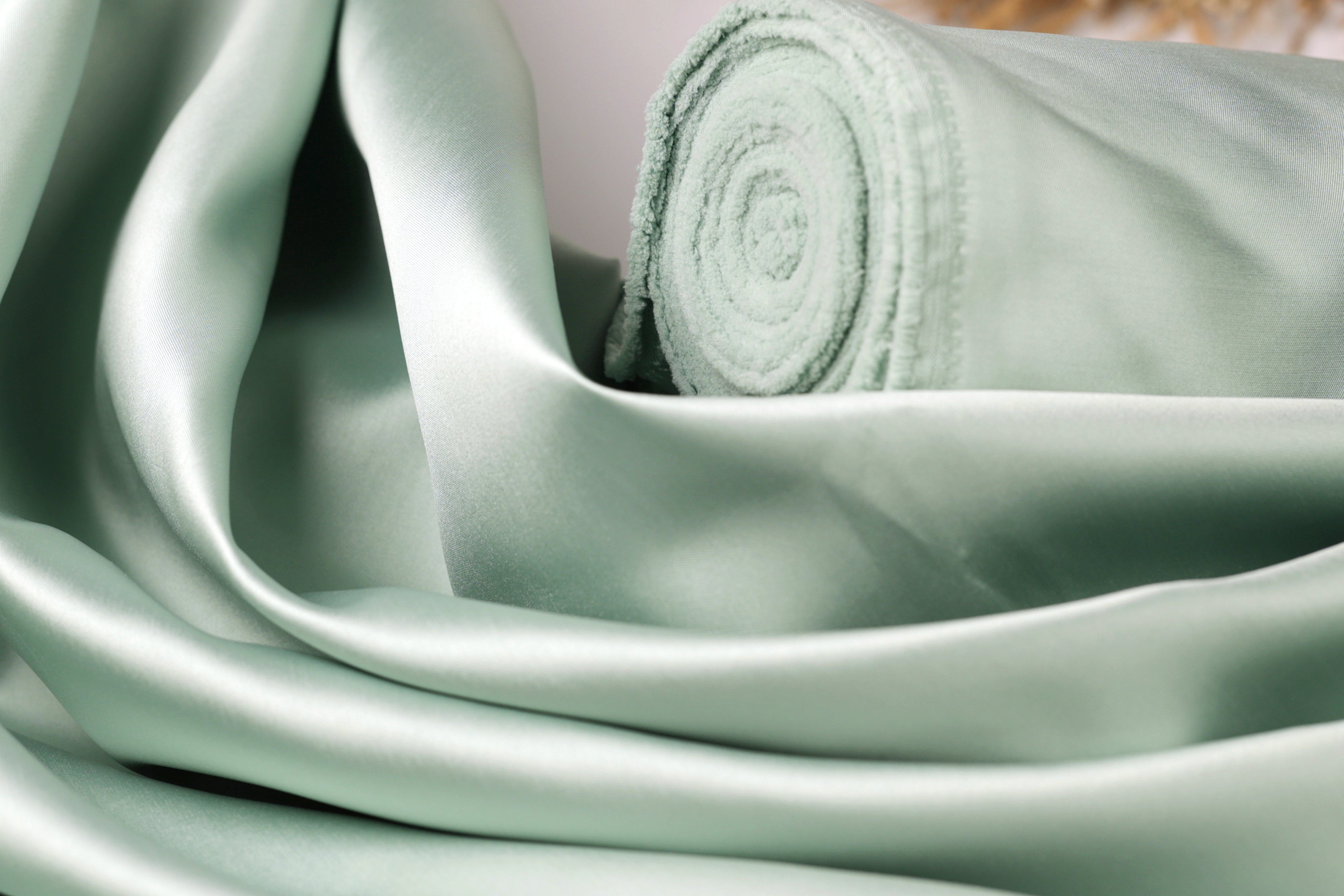 A close-up view of a piece of green satin fabric, with a rolled-up end visible.