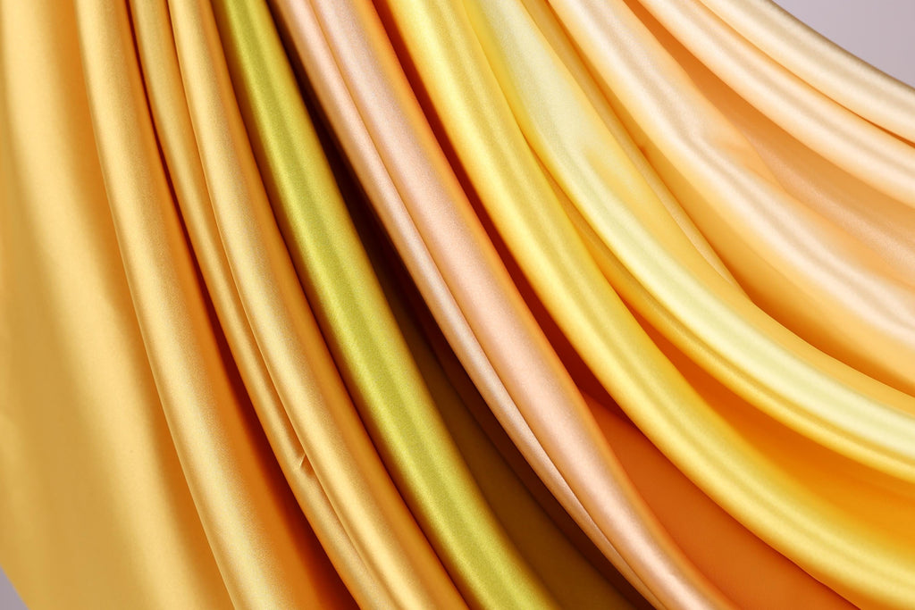 a close-up view of a variety of colorful, flowing fabrics, including yellow, orange, and green, arranged in a visually appealing manner.