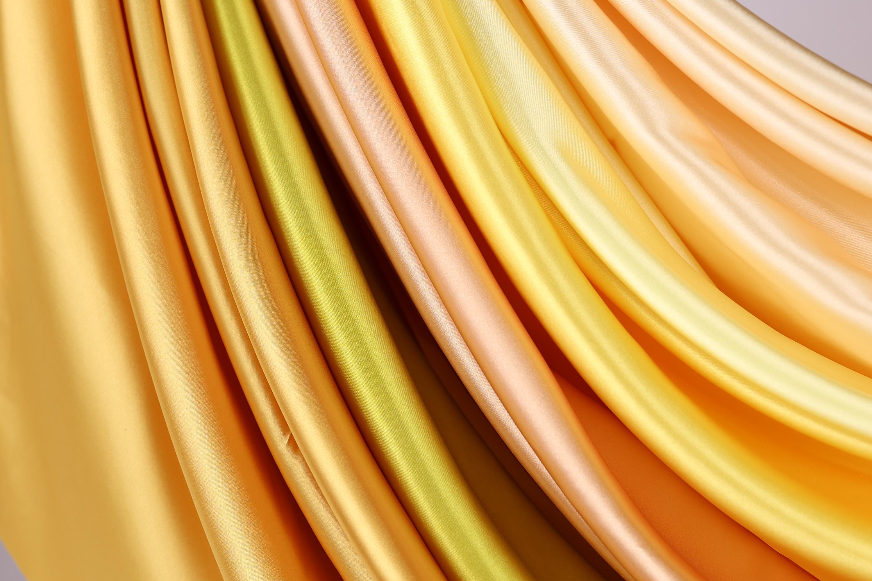 a close-up view of a variety of colorful, flowing fabrics, including yellow, orange, and green, arranged in a visually appealing manner.