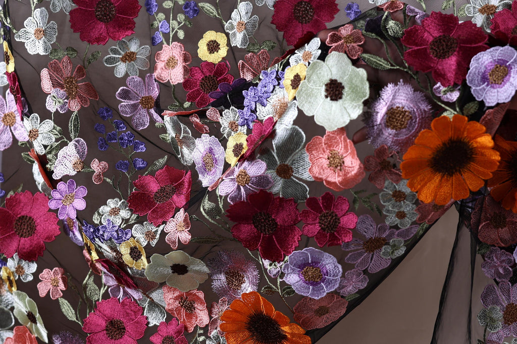 The image is a close-up of a fabric with a vibrant and intricate floral pattern, featuring a variety of colorful flowers such as red, orange, purple, and white.