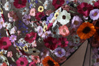 The image is a close-up of a fabric with a vibrant and intricate floral pattern, featuring a variety of colorful flowers such as red, orange, purple, and white.