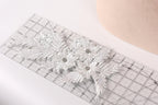 a close-up view of a white lace flower with a diamond-like center, placed on a ruler.