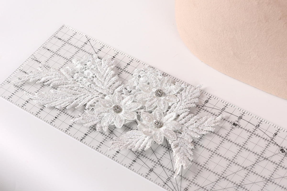 a close-up view of a white lace flower with a diamond-like center, placed on a ruler.