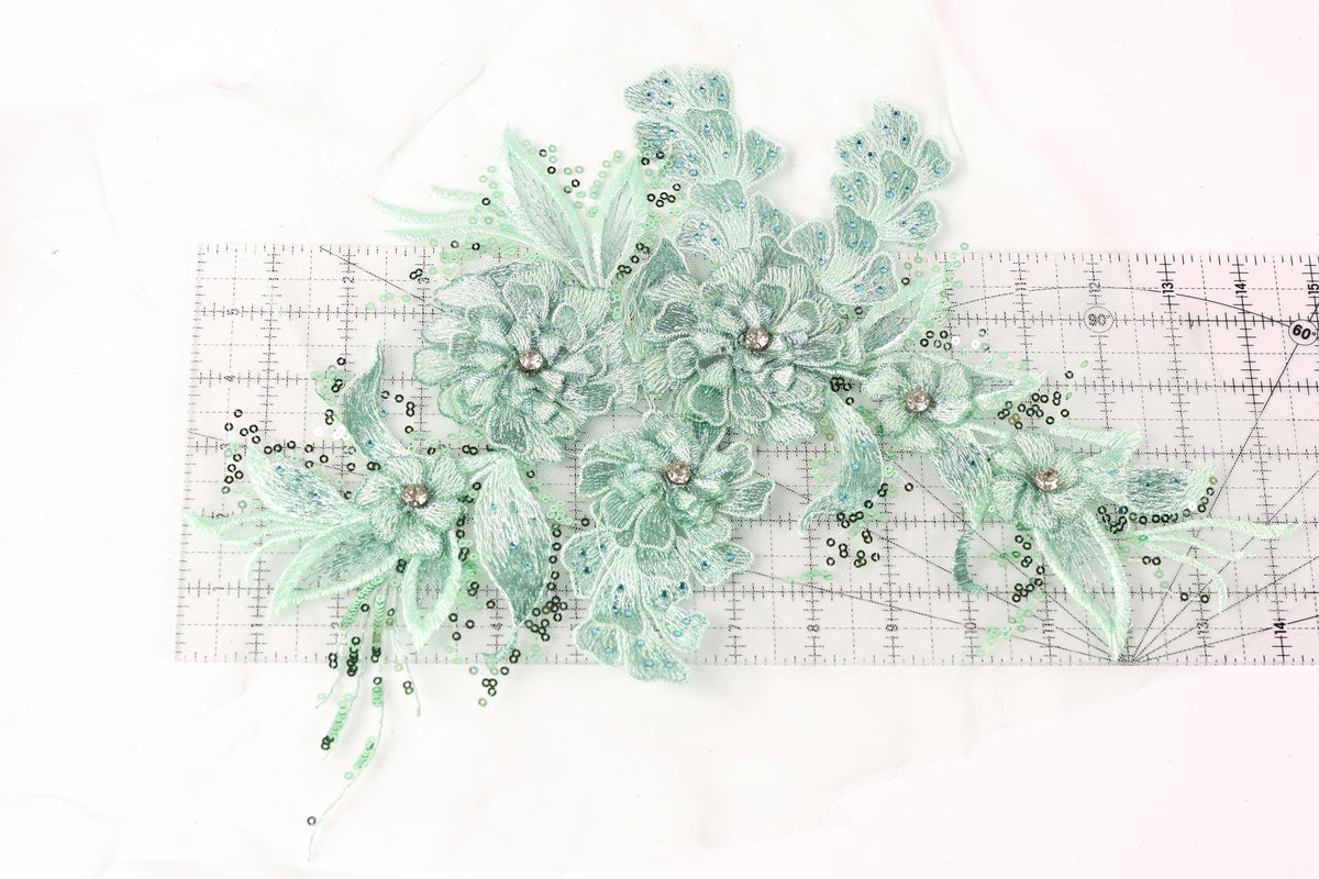 a collection of green floral embroidery pieces, including flowers and leaves, arranged on a ruler for scale.