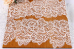 a close-up view of a wooden surface adorned with intricate white lace patterns. The lace appears to be hand-stitched and has a delicate, ornate design. The wooden surface is positioned in the center of the image, drawing attention to the lace patterns. The background is blurred, keeping the focus on the lace and the wooden surface.