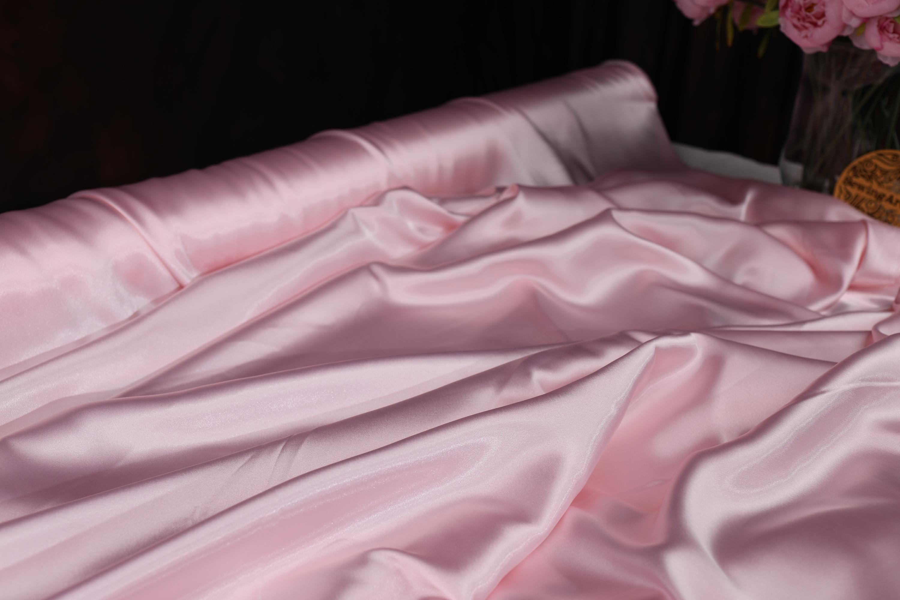 a vase of pink flowers sitting on top of a bed